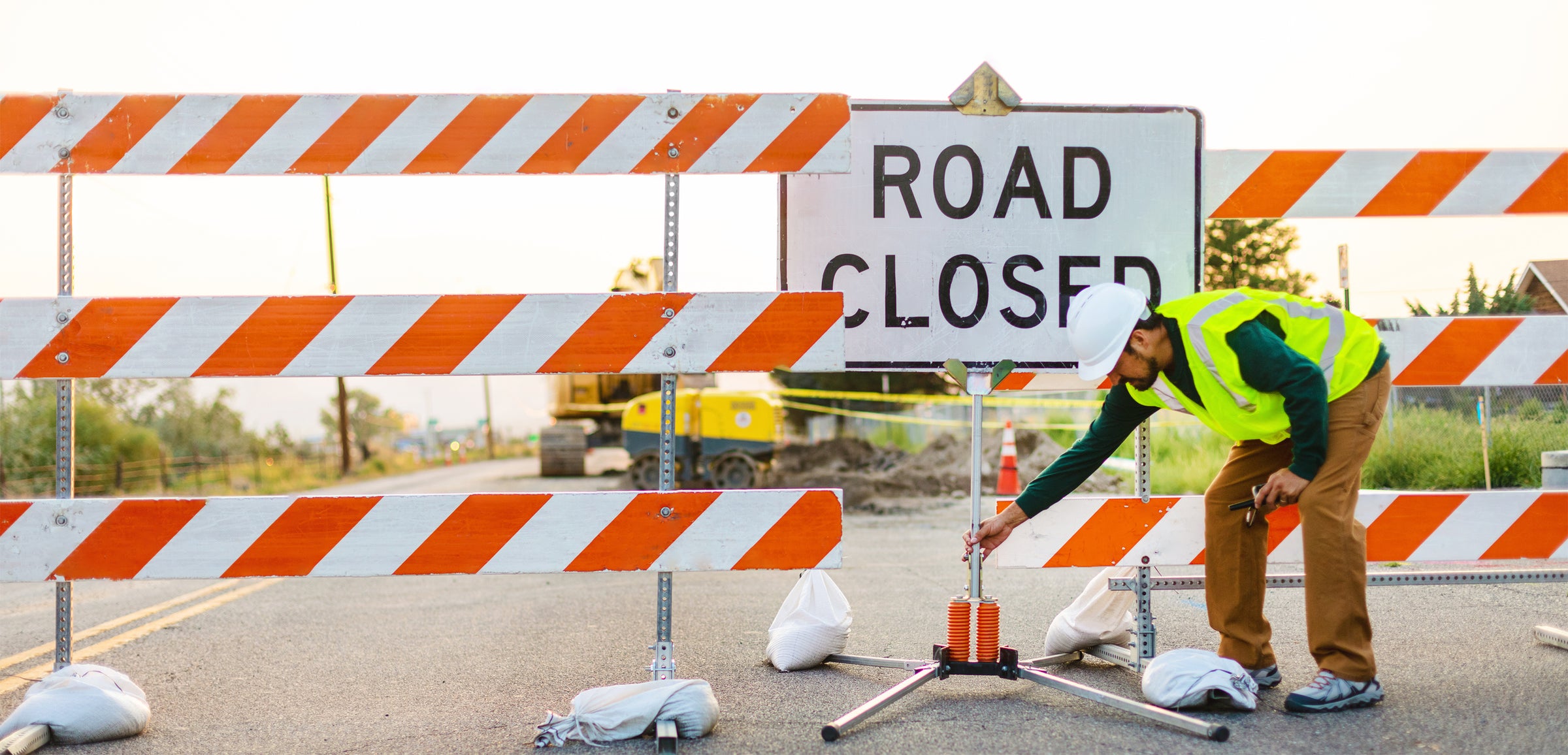 Worker Setting Up Barricades and Road Closed Sign Image